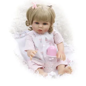 Detail of reborn baby doll with blonde curls, pink bows, and cherry outfit near a bottle