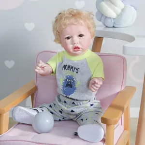 Lifelike reborn boy doll Saskia with curly blonde hair sitting on a pink mini sofa