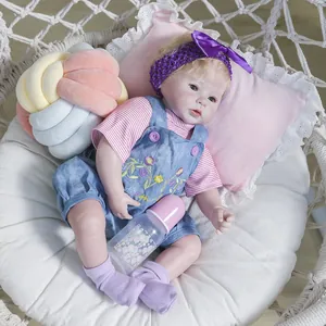 Poupée reborn réaliste de 50cm avec cheveux blonds en salopette fleurie sur coussin rose