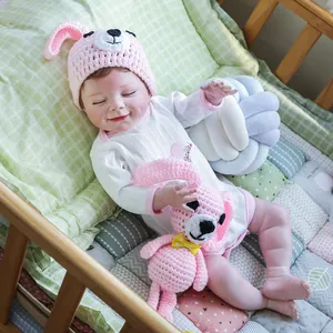 Bambola reborn realistica April da 22 pollici con cappello rosa e tutina bianca
