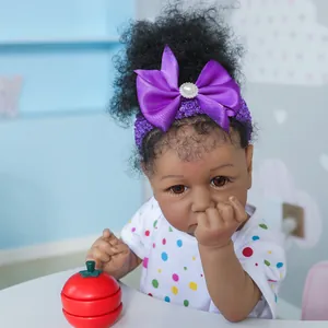 Poupée Reborn Saskia 55cm à peau foncée en body blanc à pois avec bandeau nœud violet
