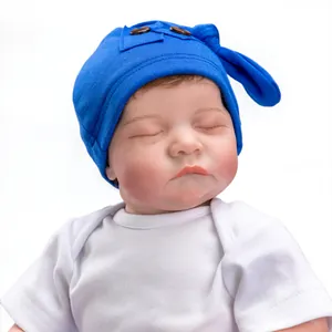 Close-up of sleeping reborn Levi doll wearing a blue knit hat with wood buttons
