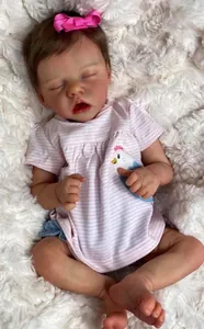 Close-up of 18-inch sleeping reborn doll in pink striped outfit on white faux fur