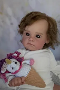 Close-up of 60cm reborn doll with realistic curly brown hair holding a crochet unicorn toy