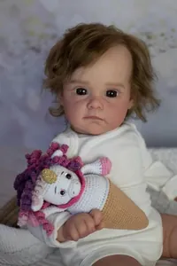 Close-up of 60cm reborn baby doll Maggi with brown curls and hand-knitted unicorn toy