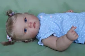 Close-up of lifelike reborn doll Charlotte with blonde pigtails and blue polka dot dress