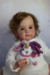 Close-up of 60cm reborn doll Maggi with brown curls holding a crochet unicorn toy