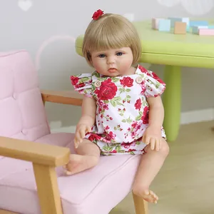 Poupée Reborn réaliste de 48 cm en vinyle avec cheveux blonds et robe à fleurs sur une chaise