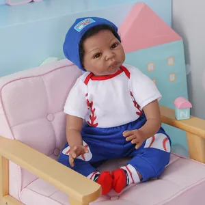 Poupée bébé noir réaliste de 55 cm en tenue de baseball assise sur un canapé rose