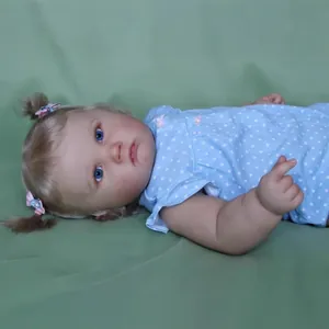 60cm Reborn Charlotte doll with blonde pigtails in blue polka dot onesie on green fabric