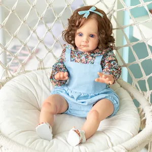 60cm Reborn Toddler Maggi doll with brown curls sitting in a white woven swing chair