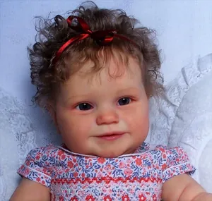 Close-up of Maddie reborn doll with curly brown hair, red bow and blue eyes