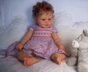 Detail of reborn toddler doll with curly brown hair and red floral dress in a cozy setting