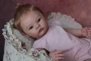 Close-up of 18-inch reborn baby doll with blonde hair, blue eyes and pink romper