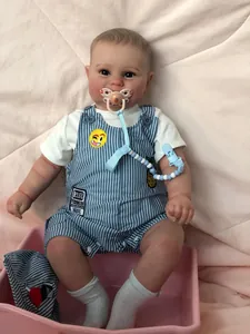 Detailed close-up of 60cm reborn baby boy doll in striped overalls sitting in a pink basket
