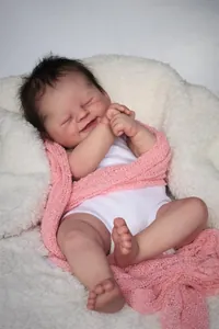 Close-up of sleeping 19-inch reborn baby doll in pink knit wrap on soft white faux fur