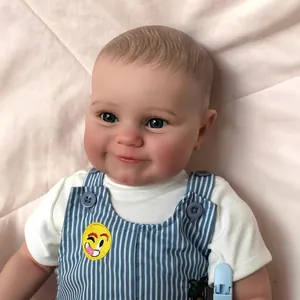 Lifelike 60cm reborn baby boy doll in blue striped overalls on a pink quilted background