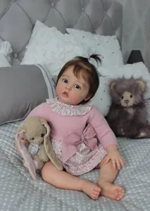 Dettaglio di una bambola reborn di 60 cm con vestito in maglia rosa e fiocco in una cameretta