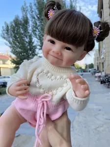 Détail d'une poupée reborn avec sourire à fossettes, cheveux bruns et pull en maille ivoire