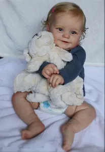 Lifelike reborn baby doll wearing a blue top and holding a plush sheep toy on a white cloth