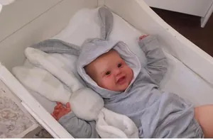 Vue détaillée d'une poupée Reborn de 60cm en sweat à oreilles de lapin dans un berceau blanc