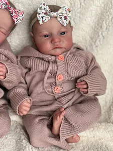 Detailed close-up of a realistic reborn baby doll in a pink knit romper with floral headband