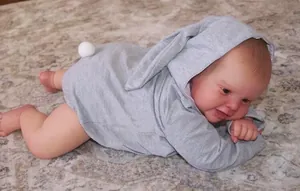 Détail d'une poupée reborn portant une barboteuse grise à capuche avec oreilles de lapin