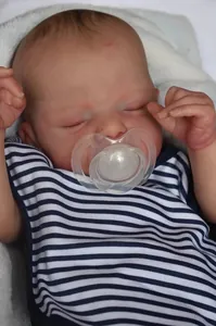 Close-up of lifelike newborn doll sleeping with pacifier and striped cotton vest