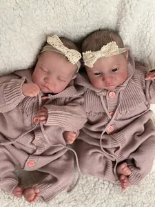 Close-up of twin newborn reborn dolls in pink knitted outfits on a soft plush backdrop
