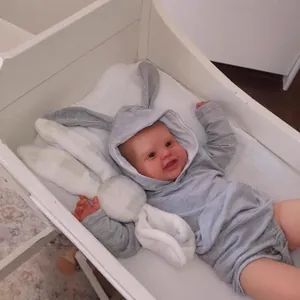 Poupée Reborn en barboteuse lapin grise à longues oreilles dans un berceau blanc