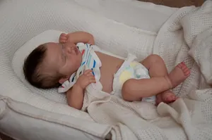 Detailed view of sleeping reborn baby doll in a bassinet with soft white blankets