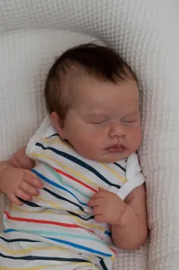 Close-up of sleeping reborn baby doll with realistic skin texture and striped outfit
