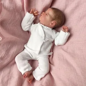 Detail of sleeping reborn baby doll in white knit clothes on pink checkered blanket