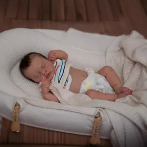 Realistic newborn baby doll in striped shirt and diaper sleeping in a white portable basket