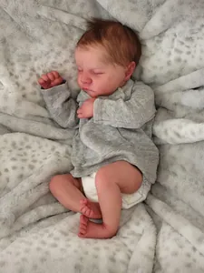 Close-up of lifelike 19-inch reborn baby doll sleeping peacefully in grey knitwear