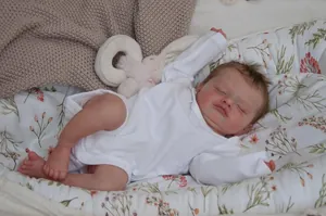 Close-up of a lifelike sleeping reborn doll in white romper on a floral nest with a bunny