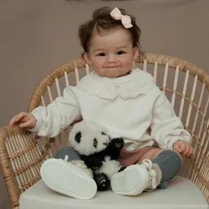 Realistic 60cm reborn baby doll with brown curls and panda toy on a wicker chair