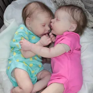 Detailed twin reborn dolls in blue lemon print and pink rompers on soft bedding