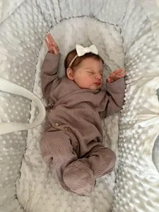 Detailed top view of 19-inch reborn baby doll in pink knitted romper on soft white fabric