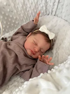 Close-up of reborn baby doll in purple knit outfit sleeping on soft white bedding