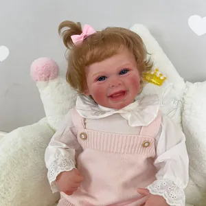 Bambola realistica da 50cm con capelli castani e vestito rosa seduta su una sedia peluche