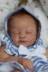 Close-up of sleeping reborn baby doll August with realistic skin texture and striped hoodie