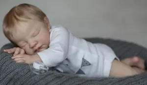 Close-up of a 19-inch sleeping reborn baby doll in white cotton onesie on a knit blanket