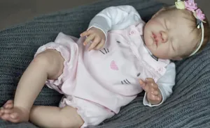 Close-up of lifelike 19-inch reborn baby doll sleeping on a grey knit blanket