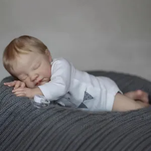 Lifelike 19-inch sleeping reborn baby doll in white romper on a soft grey knit cushion