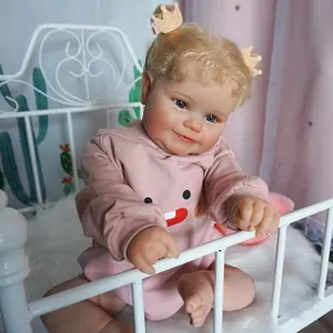 Ρεαλιστική κούκλα μωρό Maddie 60cm με ξανθές μπούκλες και ροζ πουλόβερ σε μια κούνια