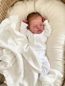 Realistic reborn baby doll in white romper lying in a natural woven basket