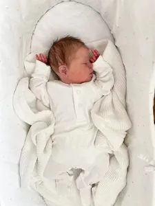 Close-up of 49cm newborn reborn doll Demi in white bodysuit on soft knitted blanket