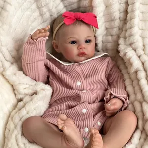 Poupée Reborn réaliste de 18 pouces avec barboteuse rose et nœud rouge sur tapis blanc