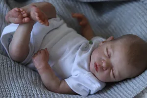 Close-up of sleeping reborn doll with realistic skin texture on grey knit blanket